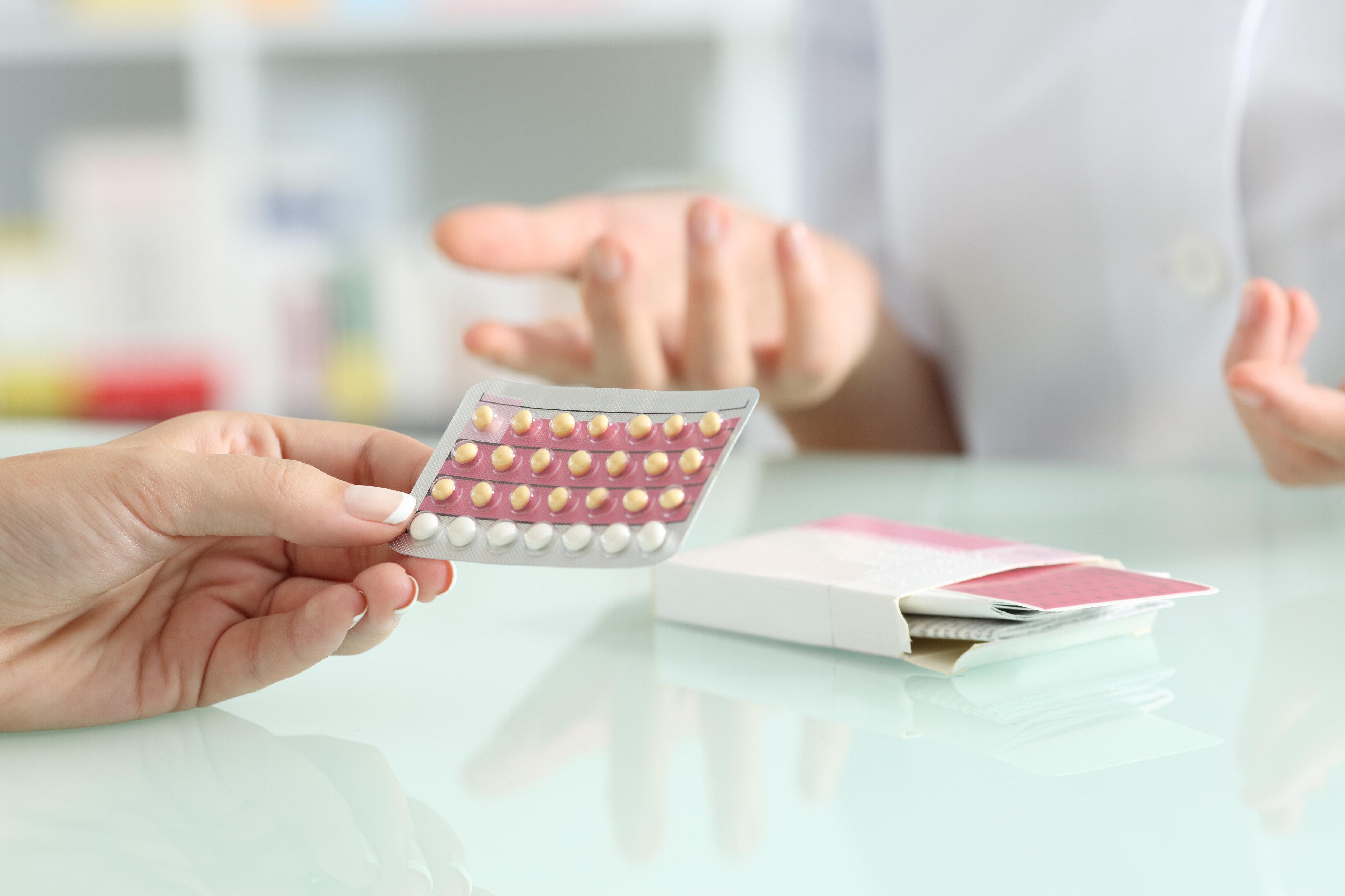 A imagem mostra duas mãos, uma delas segurando uma cartela de remédio contraceptivo.