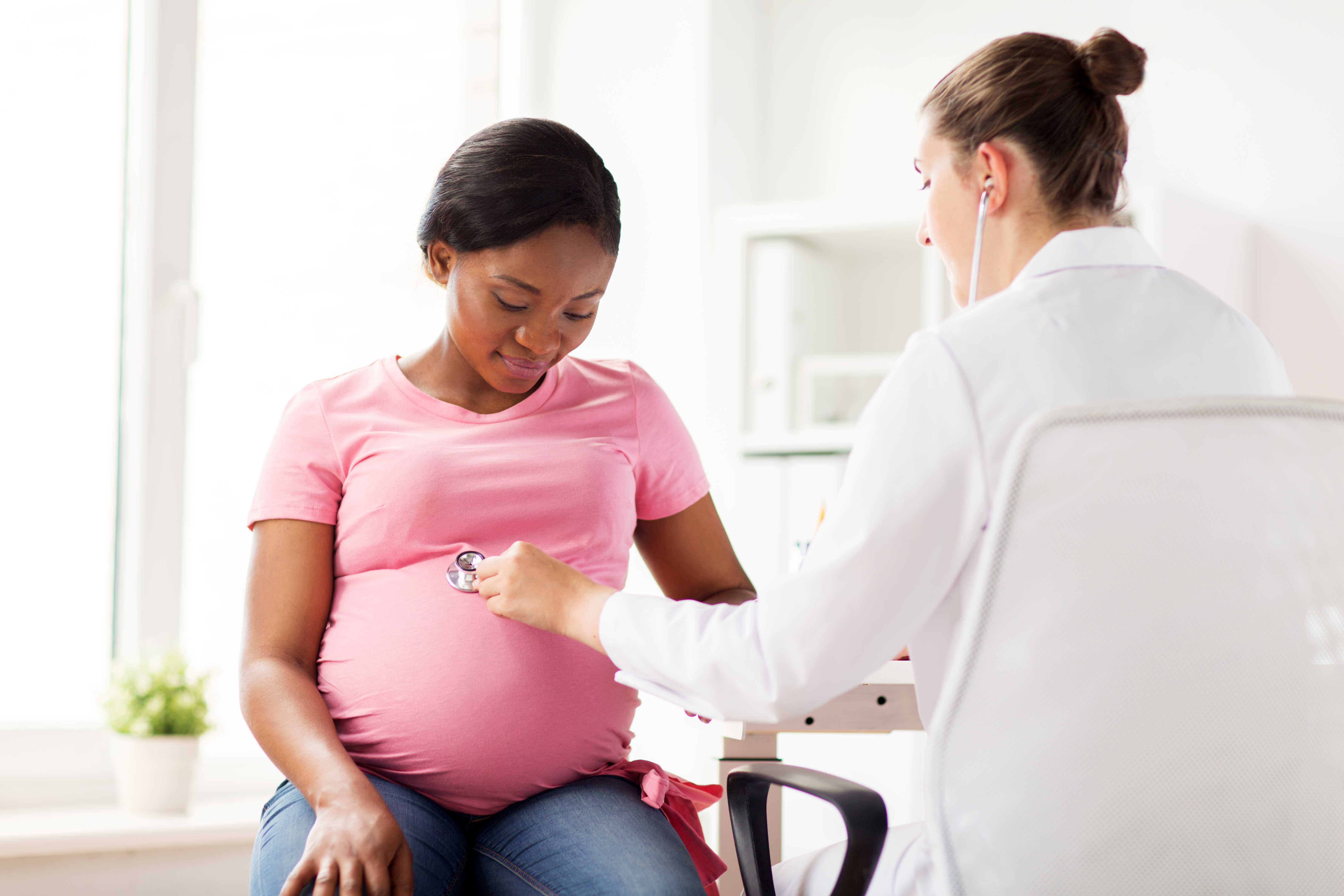 A imagem mostra uma mulher grávida sendo avaliada por uma médica.