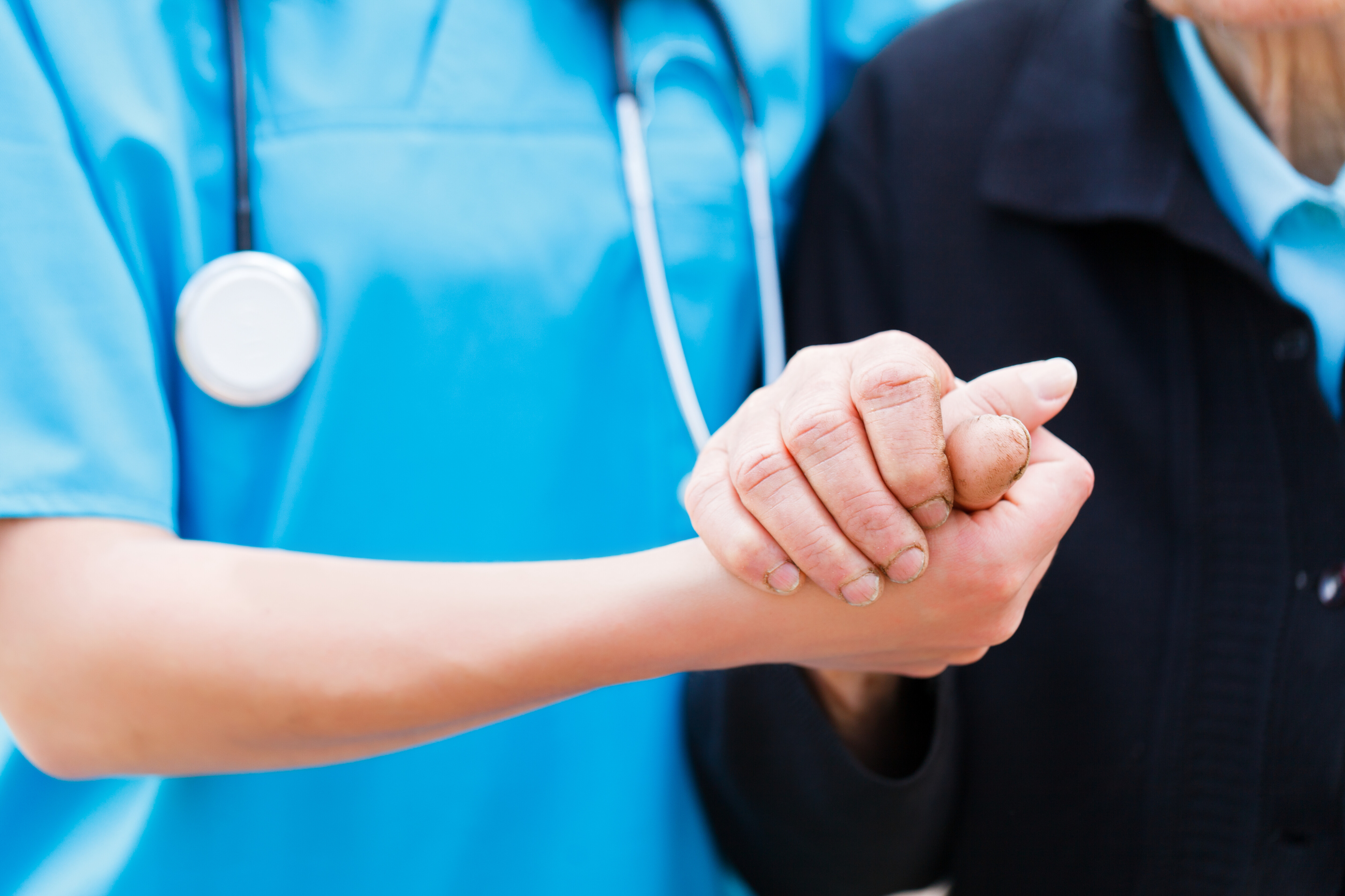 A imagem mostra um profissional da saúde de mãos dadas com um paciente idoso.